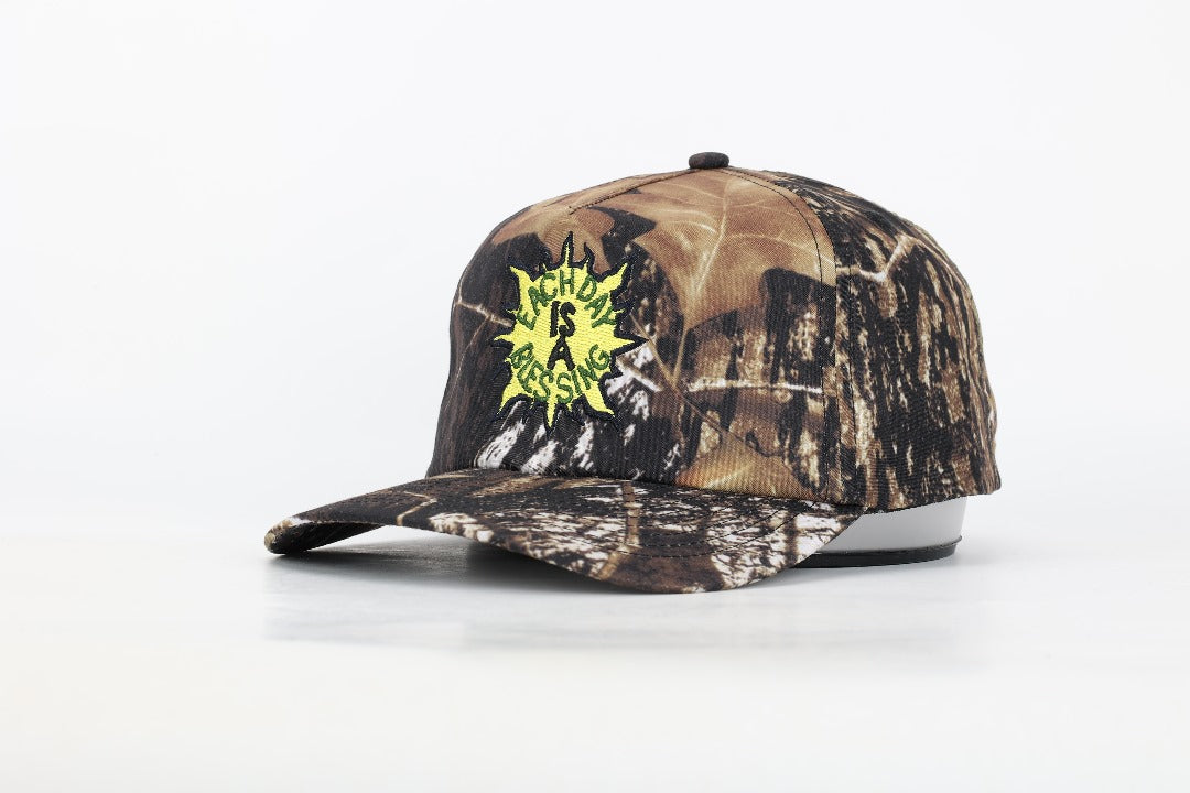 EACH DAY IS A BLESSING™ CAMO TRUCKER HAT (LEFT SIDE) BY OUR AGENCY OY