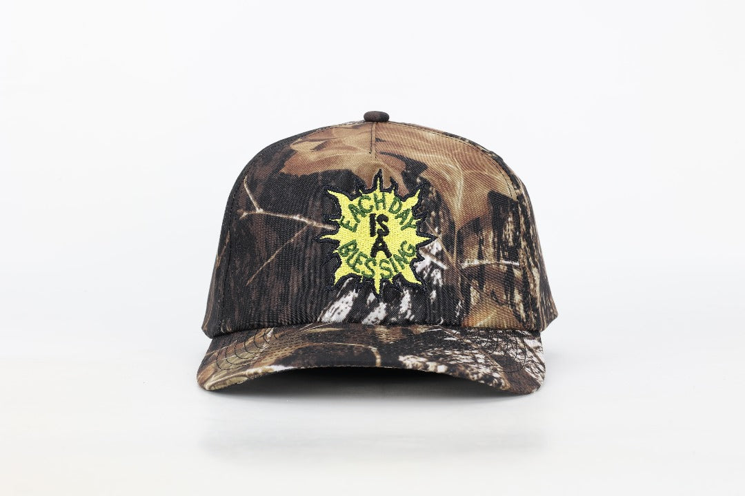 EACH DAY IS A BLESSING™ CAMO TRUCKER HAT (FRONT) BY OUR AGENCY OY